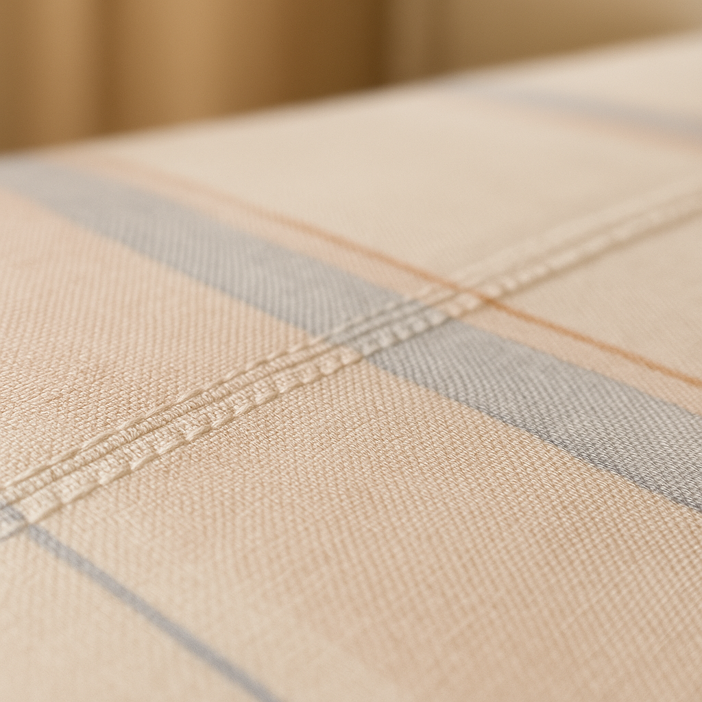 Close-up of a beige fabric with plaid pattern and visible stitching.