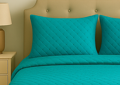 Teal quilted bedspread and pillowcases on a beige bed with a nightstand.